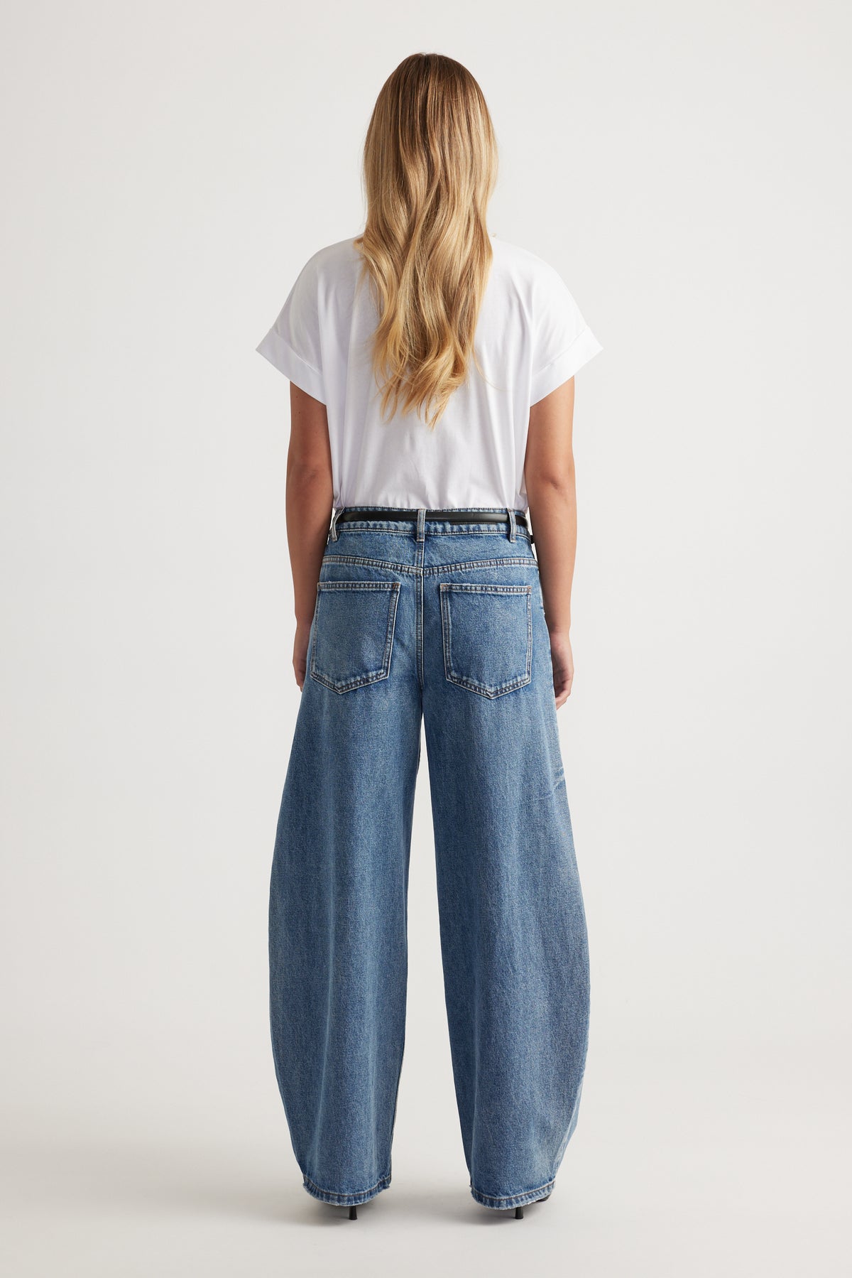 Back view of a model wearing a white crew neck tee with wide leg blue jeans