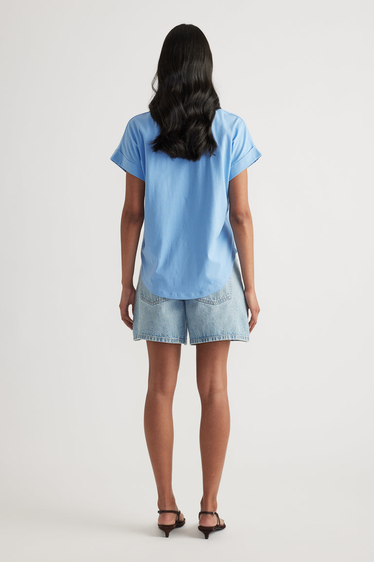 Back view of a woman wearing a blue drop shoulder tee, denim shorts and black heeled sandals