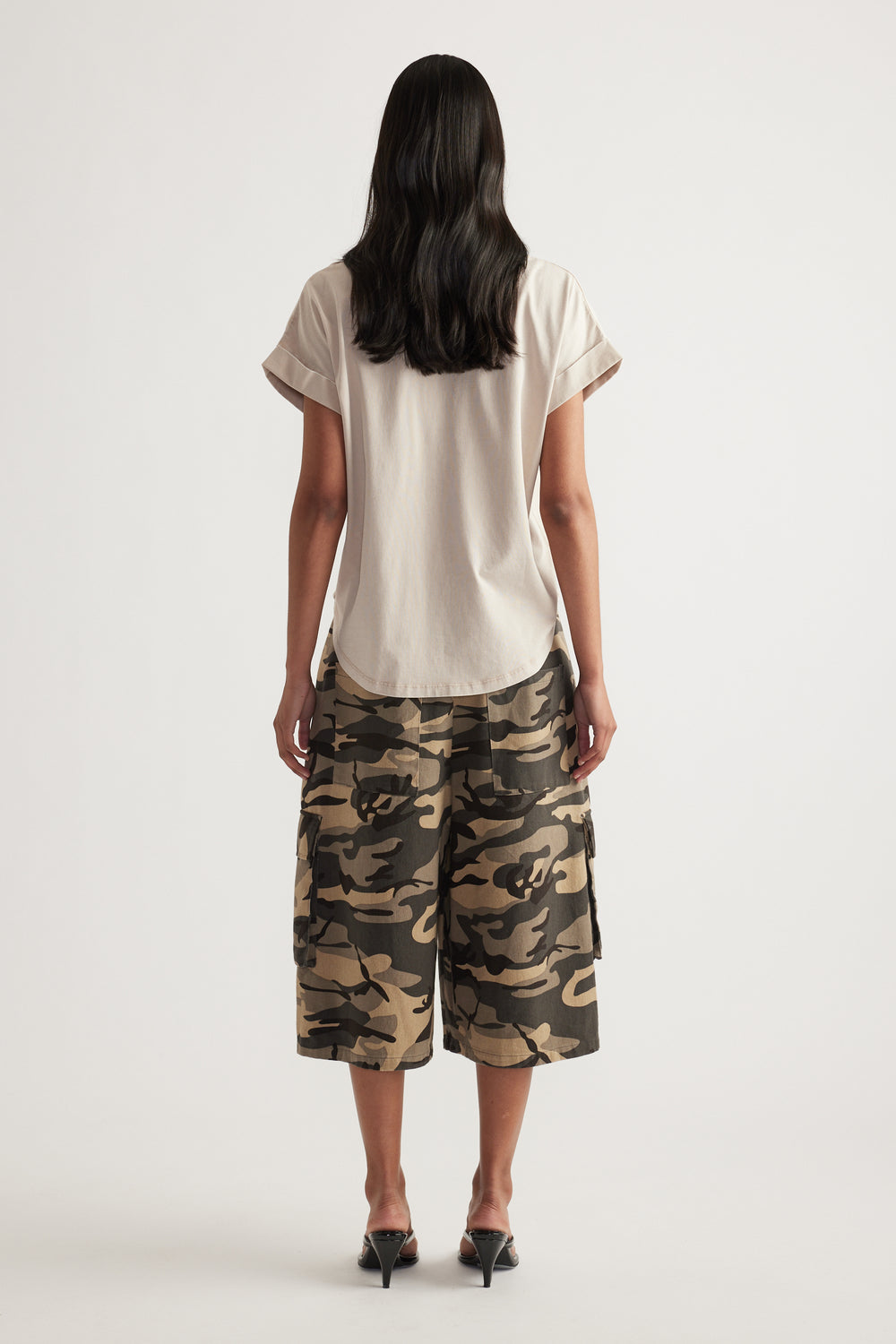 Woman viewed from behind wearing a cream crew neck tee with rolled cuffs and camouflage shorts
