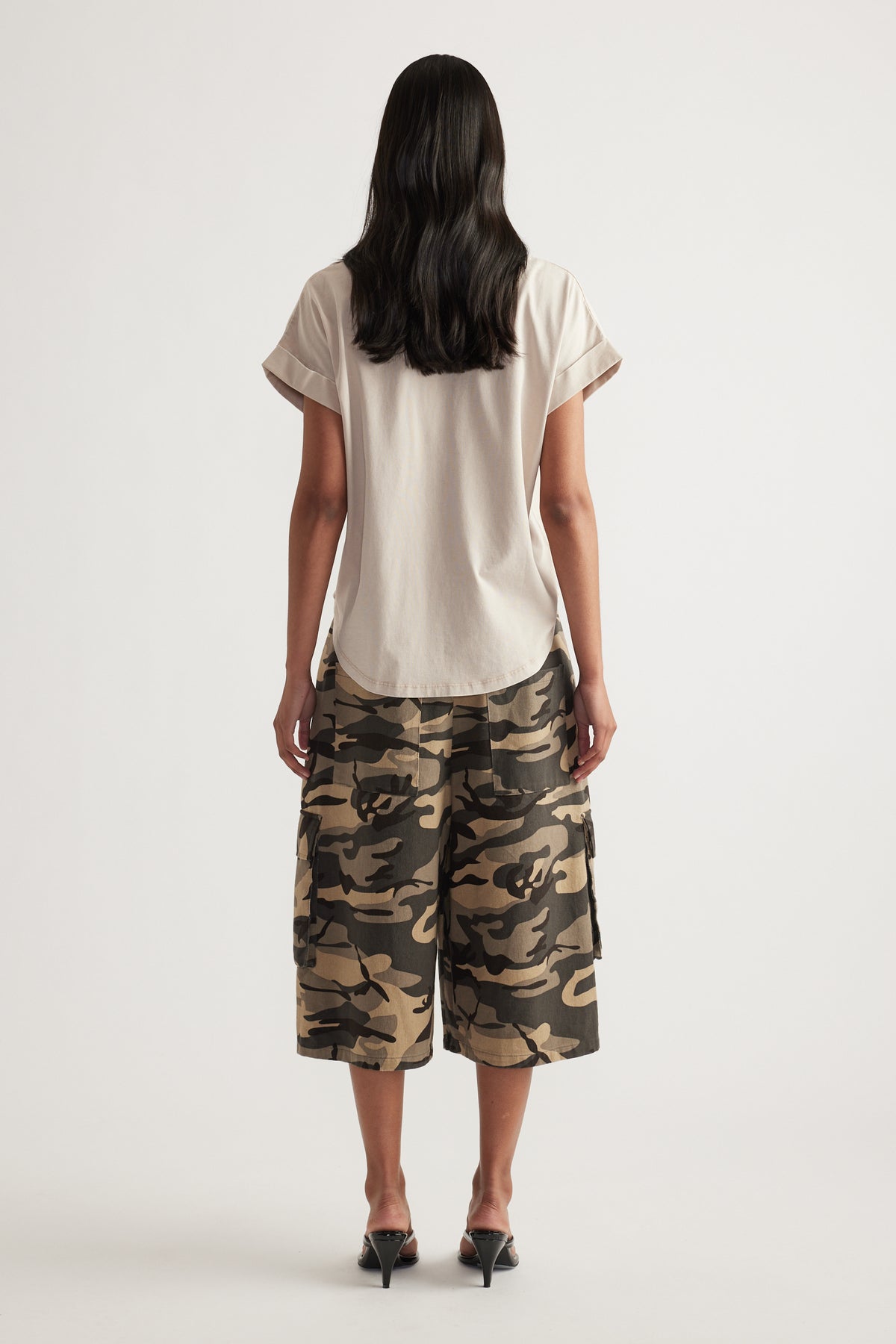 Woman viewed from behind wearing a cream crew neck tee with rolled cuffs and camouflage shorts