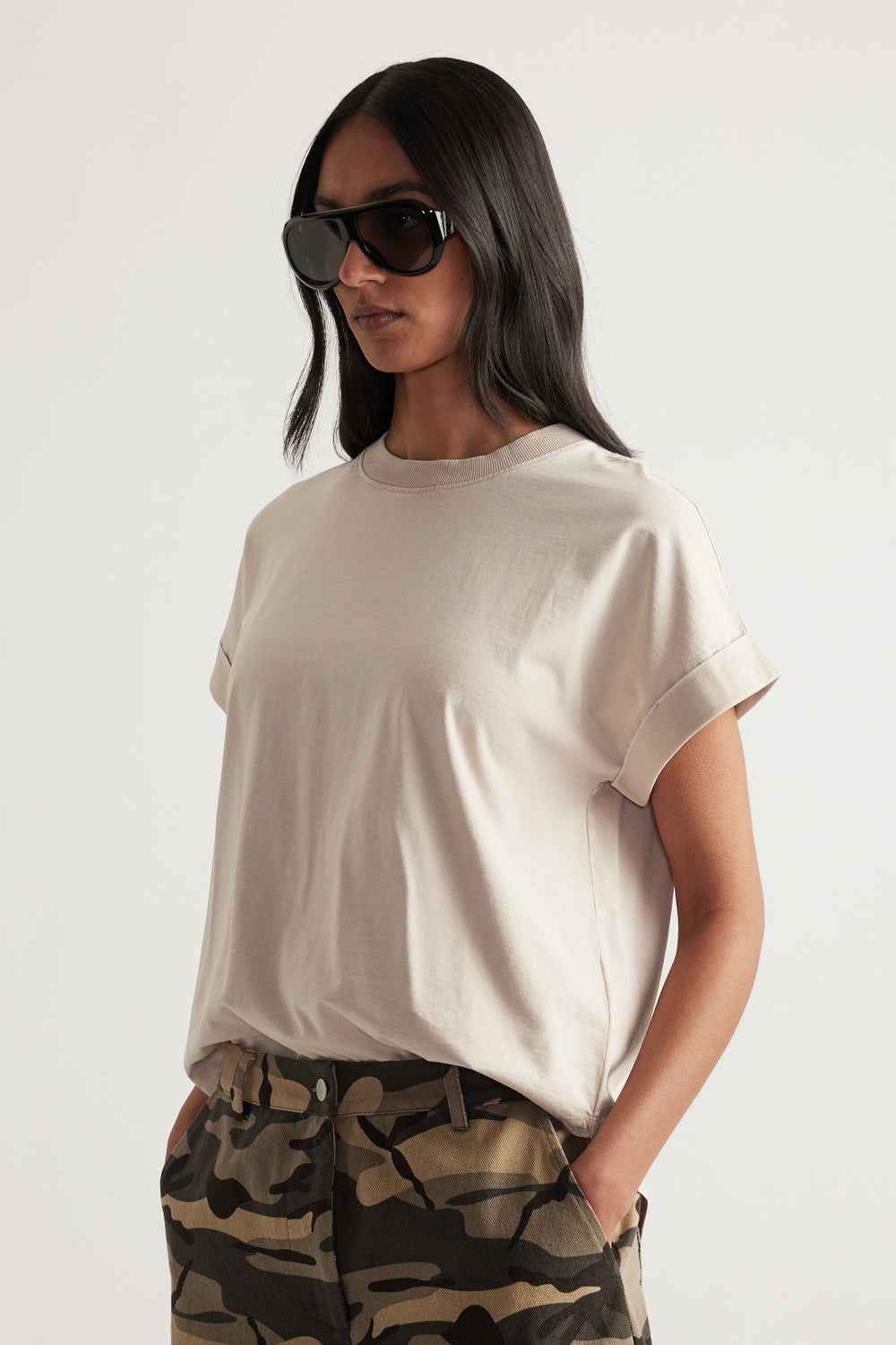 Woman wearing an off-white crew neck tee with rolled cuffs, camouflage pants and sunglasses
