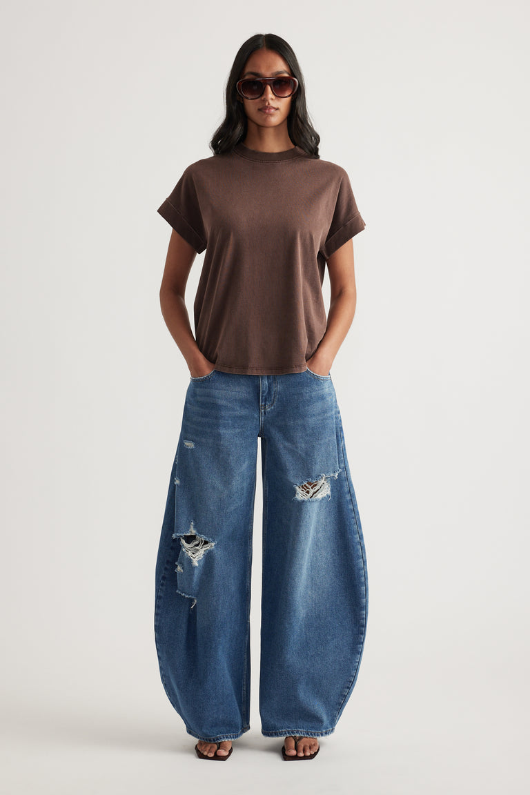 Woman in a brown crew neck tee, distressed blue wide leg jeans, sunglasses and sandals
