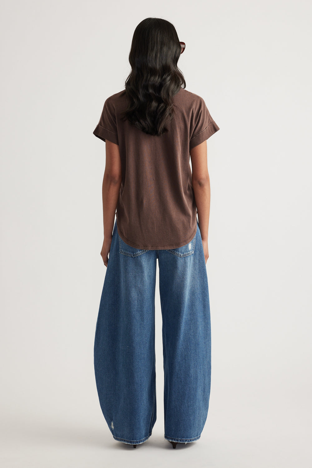 Back view of a woman wearing a brown crew neck tee with blue wide leg jeans