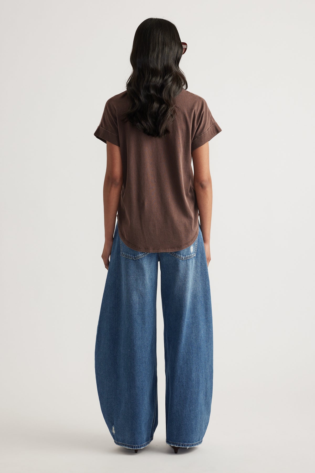 Back view of a woman wearing a brown crew neck tee with blue wide leg jeans