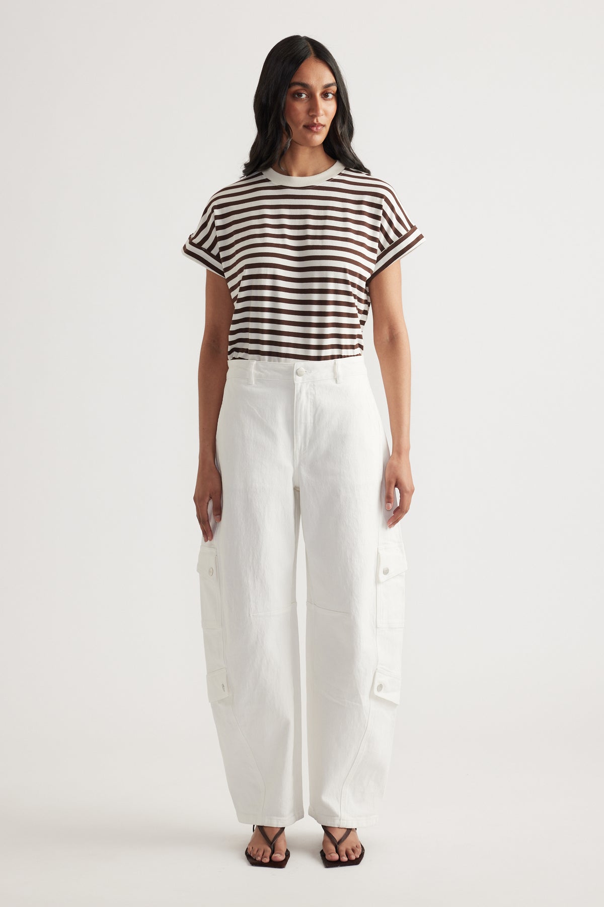 Woman wearing a brown and white striped short sleeve tee with rolled cuffs and high-waisted white wide-leg pants with pockets