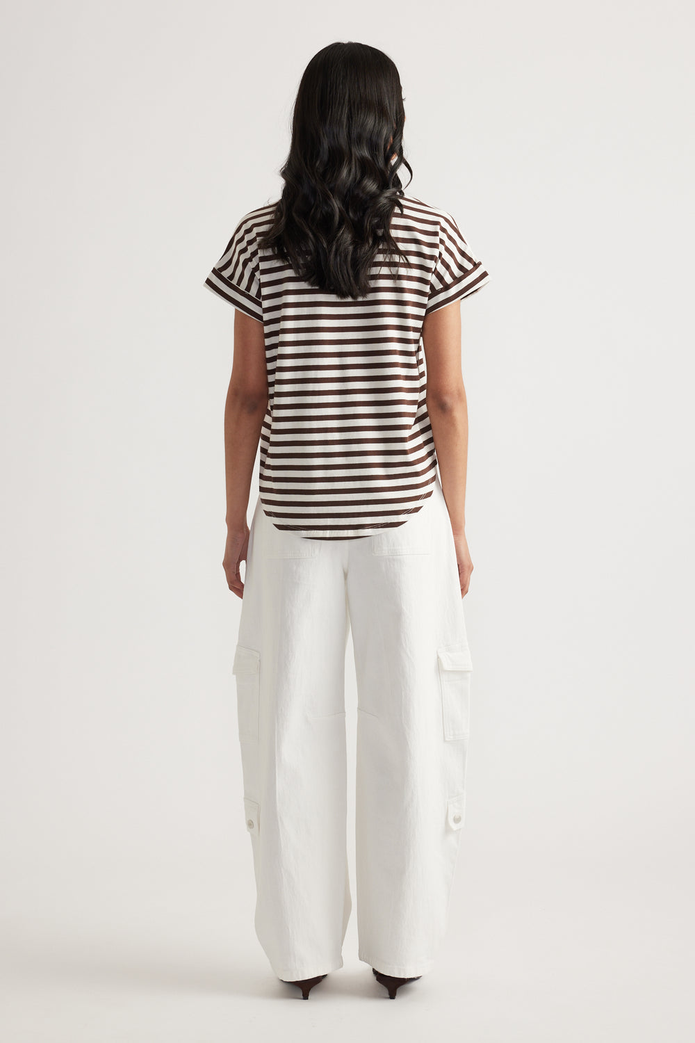 Rear view of woman wearing brown and white striped short sleeve tee paired with loose white cargo pants