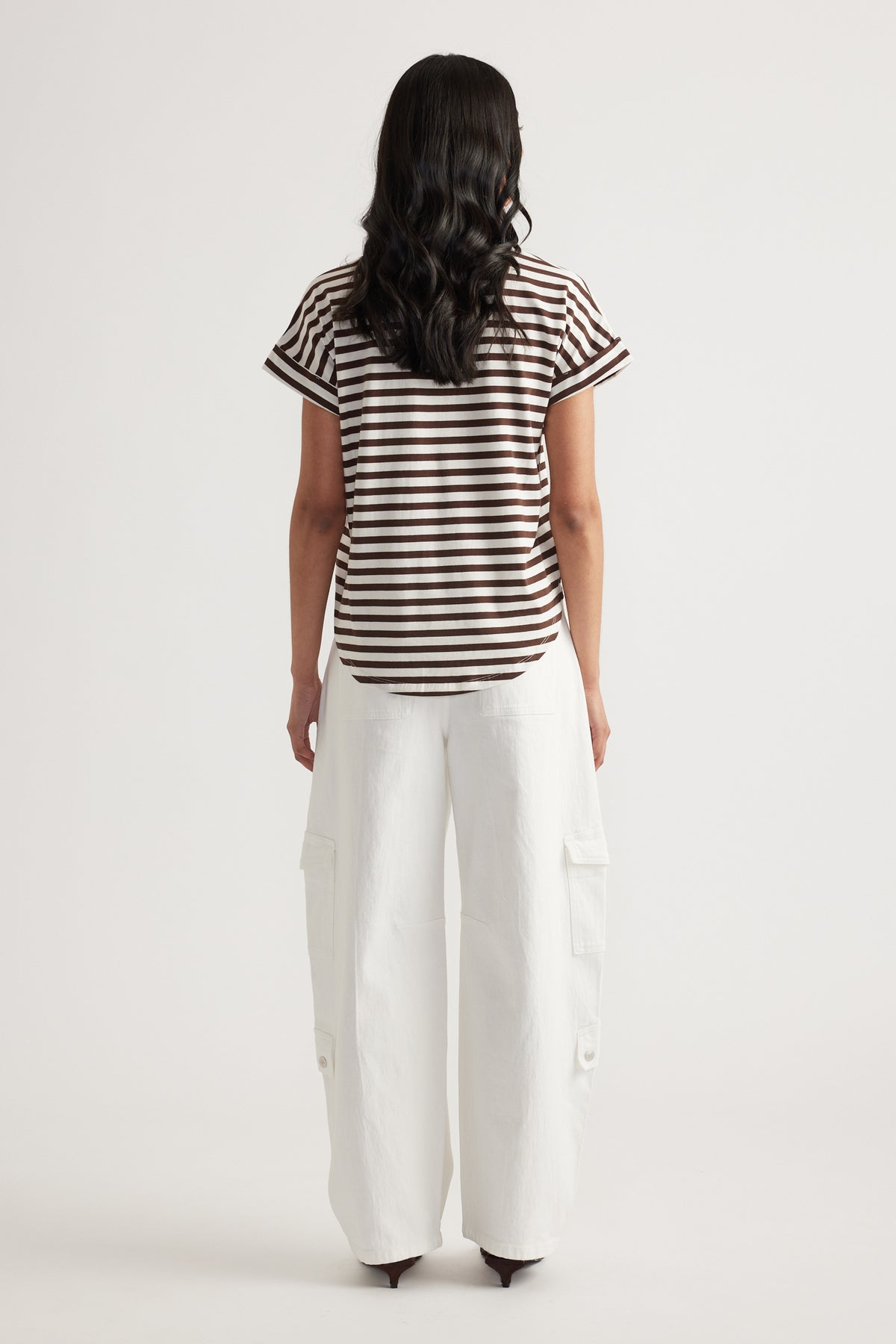 Rear view of woman wearing brown and white striped short sleeve tee paired with loose white cargo pants