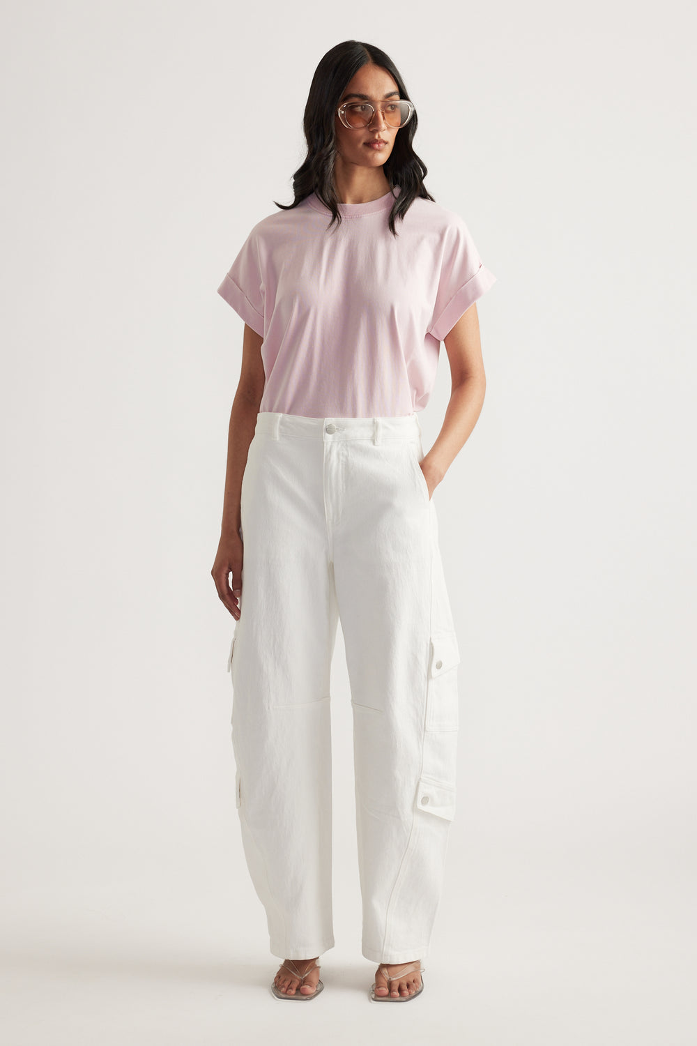 Woman wearing a pale pink crew neck tee with rolled cuffs, white cargo pants and sunglasses