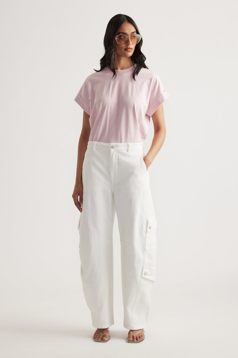 Woman wearing a pale pink crew neck tee with rolled cuffs, white cargo pants and sunglasses