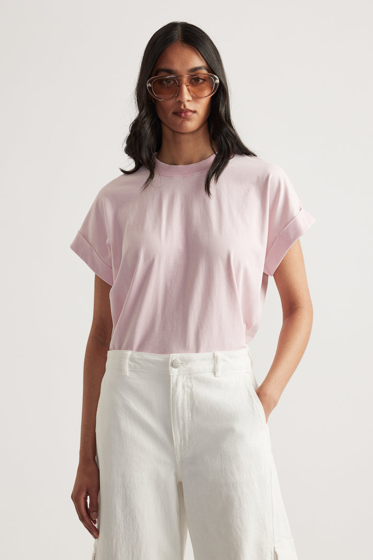 Woman wearing a soft pink crew neck tee with rolled cuffs and white high-waisted pants
