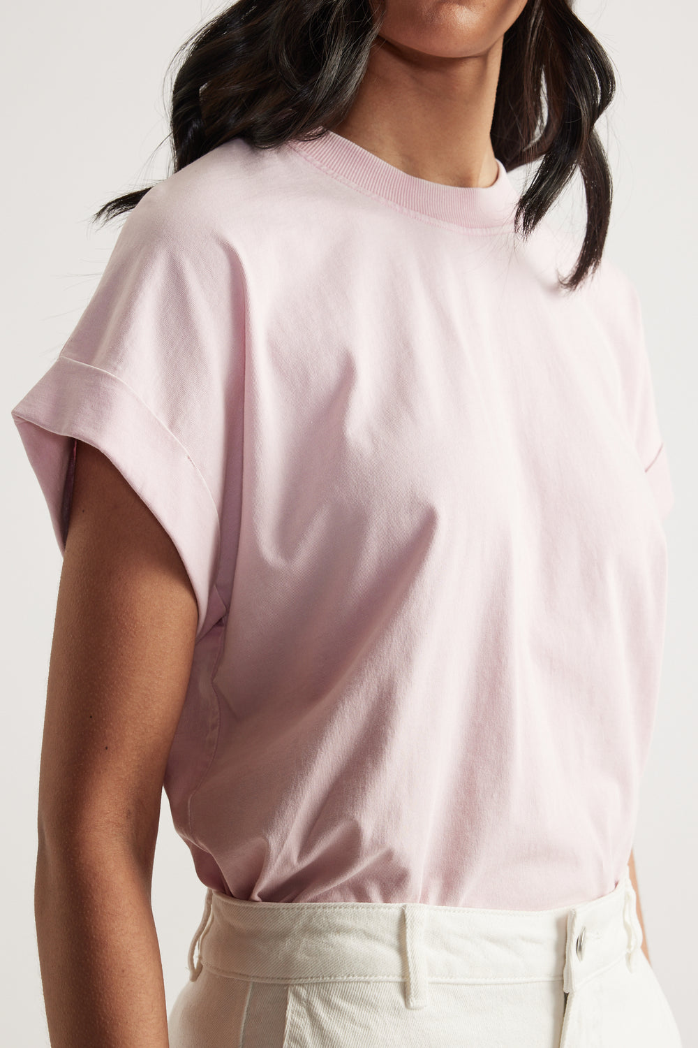 Woman wearing a pale pink crew neck tee with drop shoulders and rolled cuffs, paired with white jeans