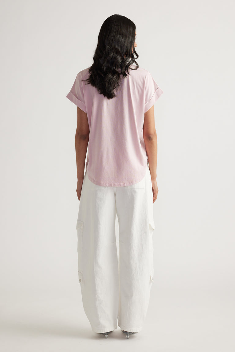 Back view of woman wearing a pale pink crew neck tee with rolled cuffs and relaxed white cargo pants