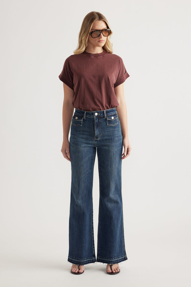 Woman in a burgundy crew neck tee with rolled cuffs and dark blue wide-leg jeans, styled with sunglasses and sandals