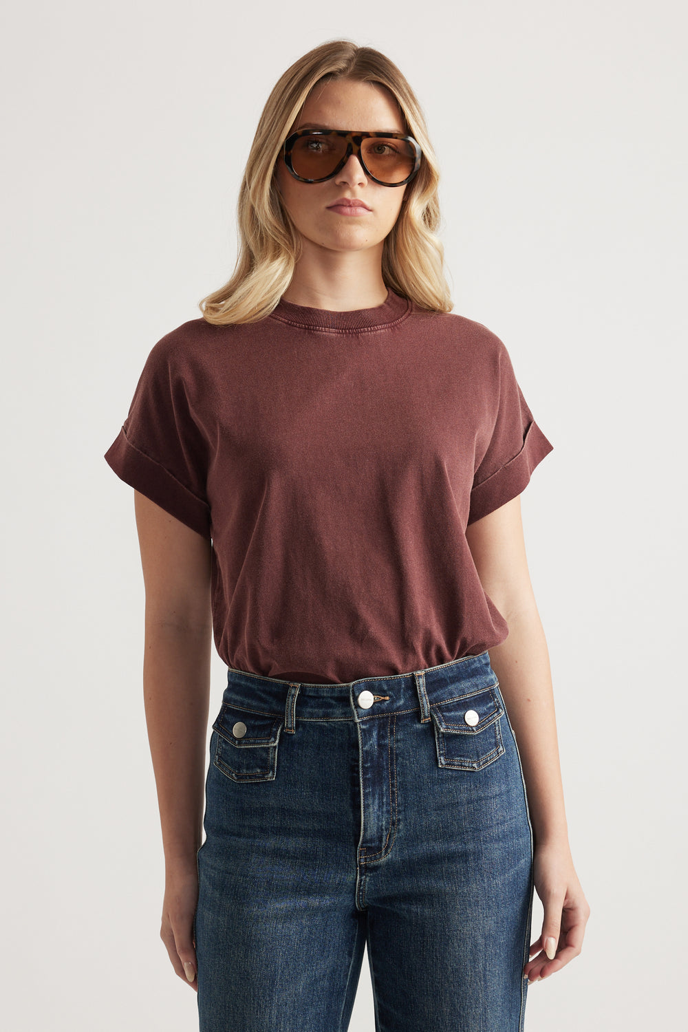 Model wearing a burgundy crew neck tee with rolled cuffs, dark blue jeans and sunglasses