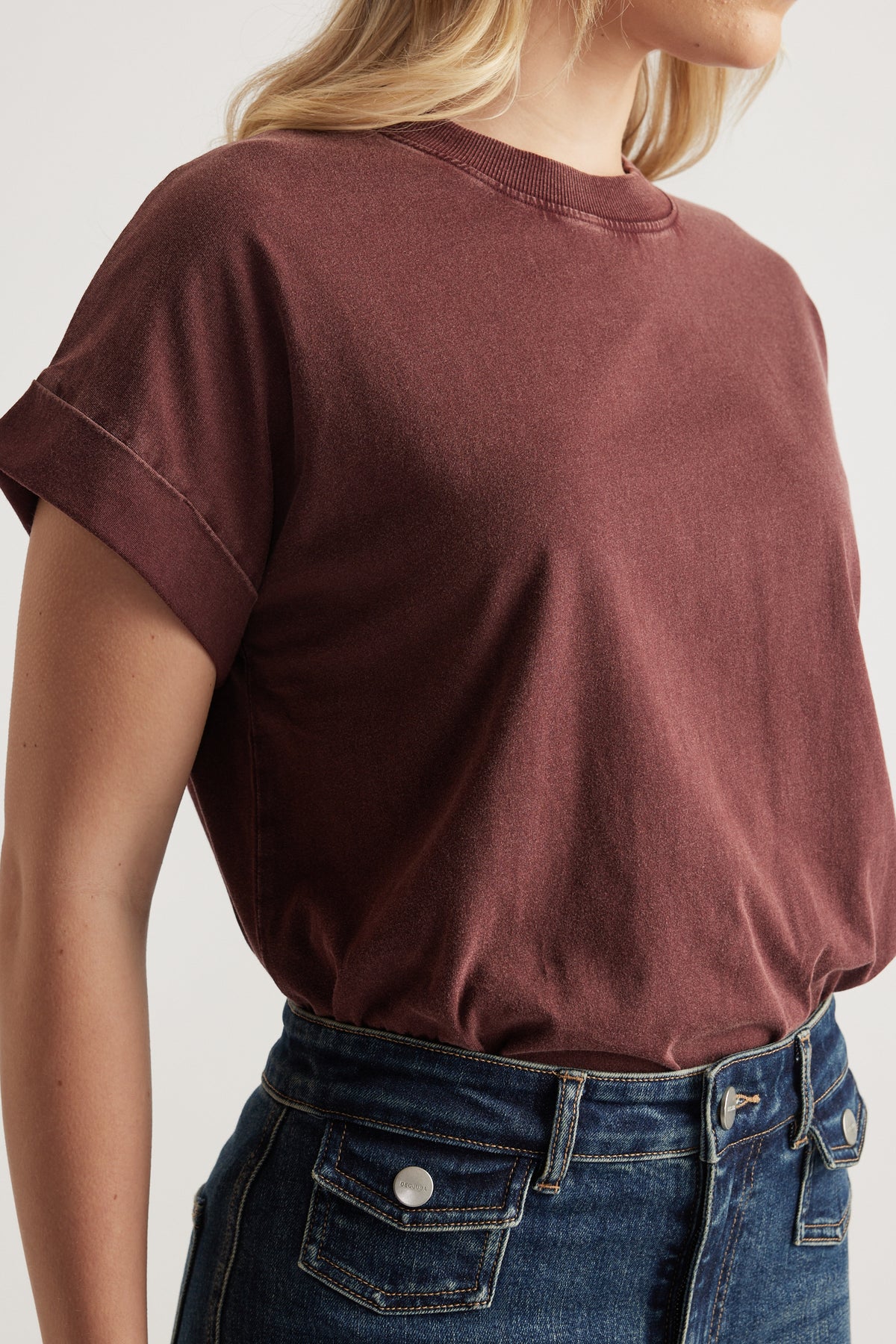 Woman wearing a brown crew neck tee with rolled cuffs and dark blue jeans