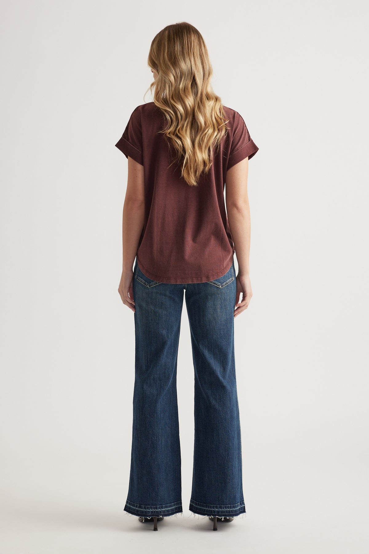 Woman wearing a burgundy crew neck tee with rolled cuffs and wide-leg blue jeans, viewed from the back