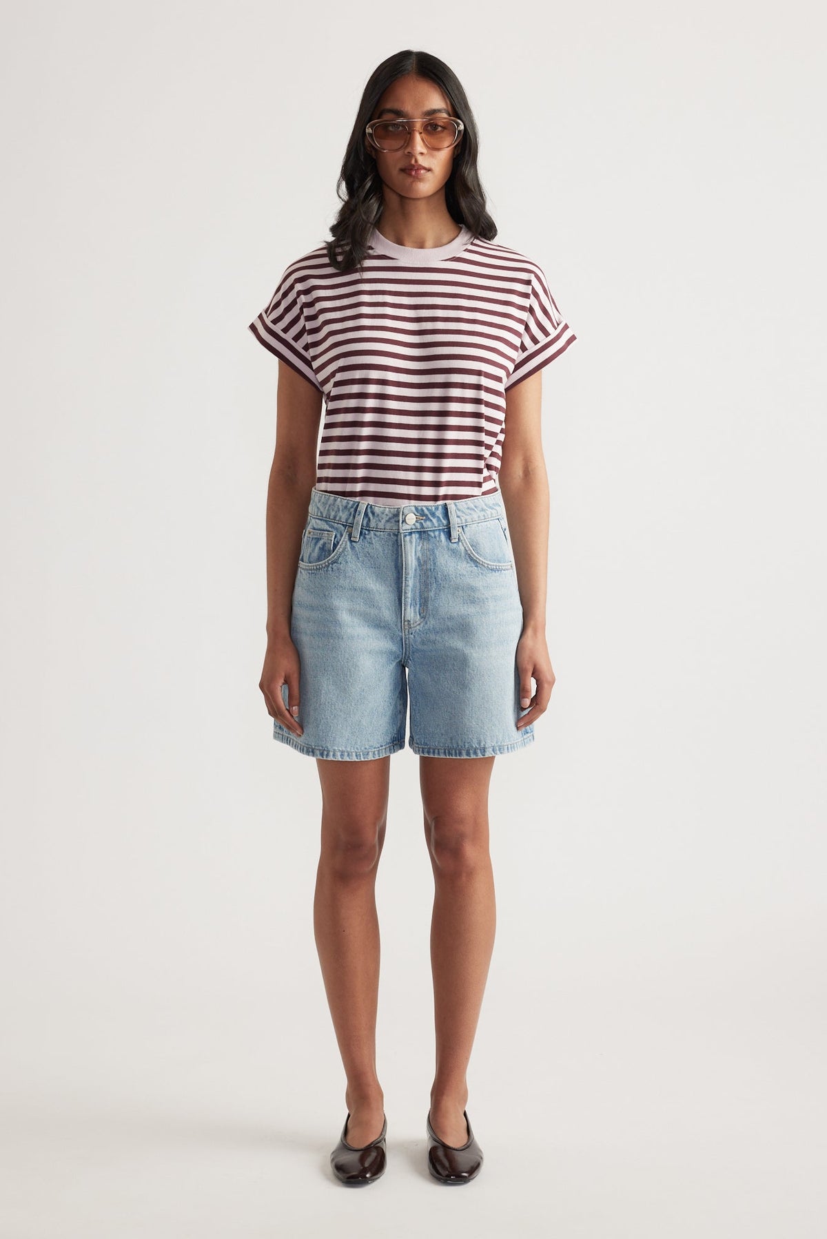 Woman wearing light blue mid-thigh denim shorts with a rolled cuff striped short sleeve tee and sunglasses