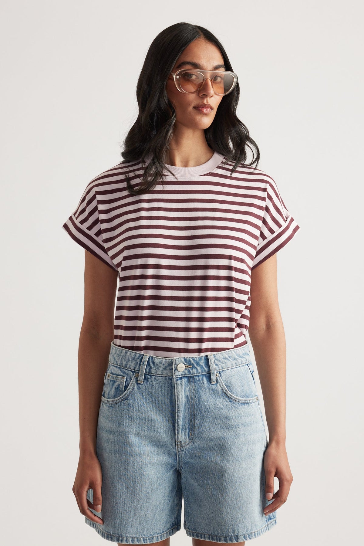 Woman wearing a maroon and white striped rolled cuff tee paired with light wash high-rise denim shorts and oversized glasses