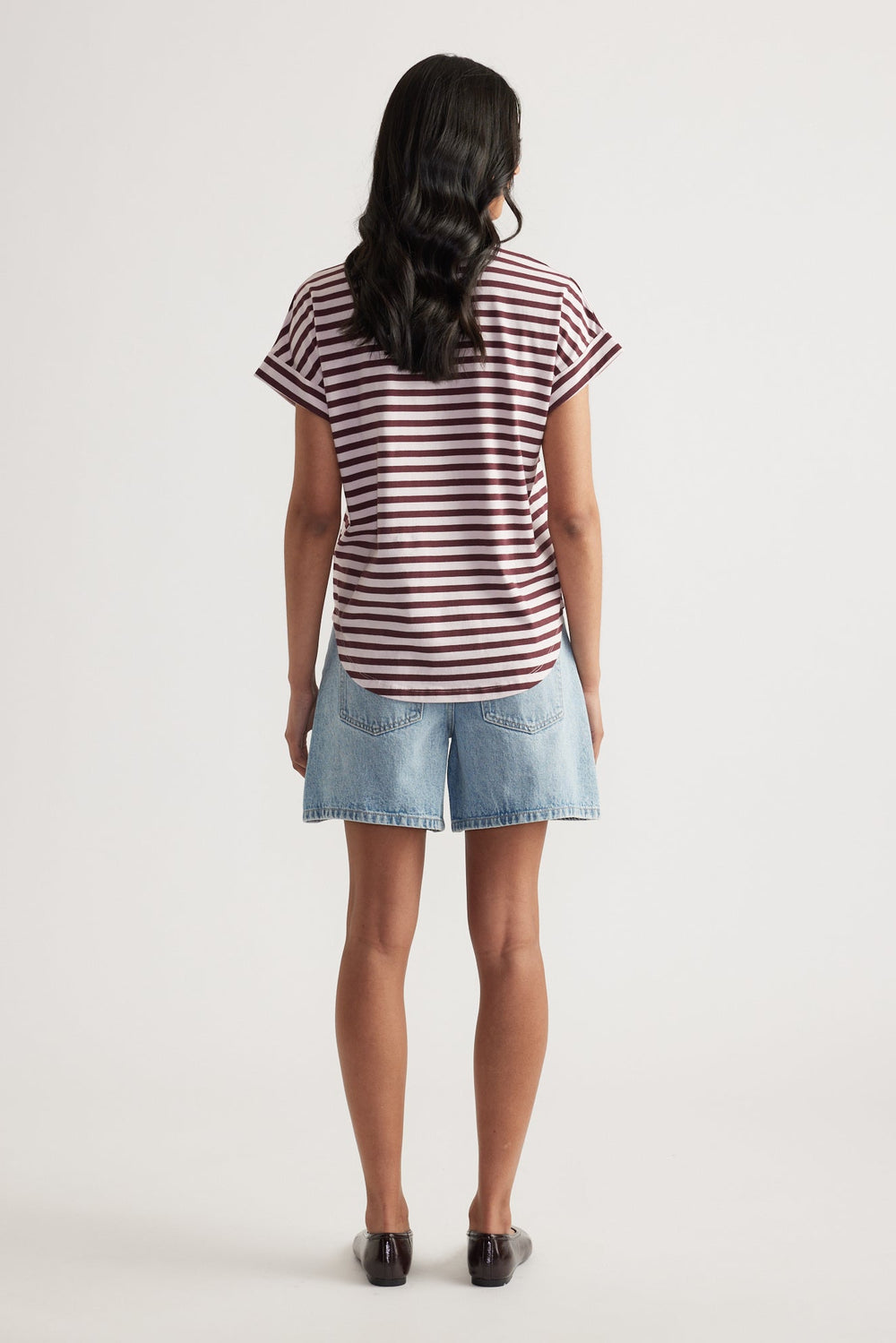 Rear view of woman wearing relaxed fit light blue denim shorts paired with a maroon and white striped rolled-cuff tee