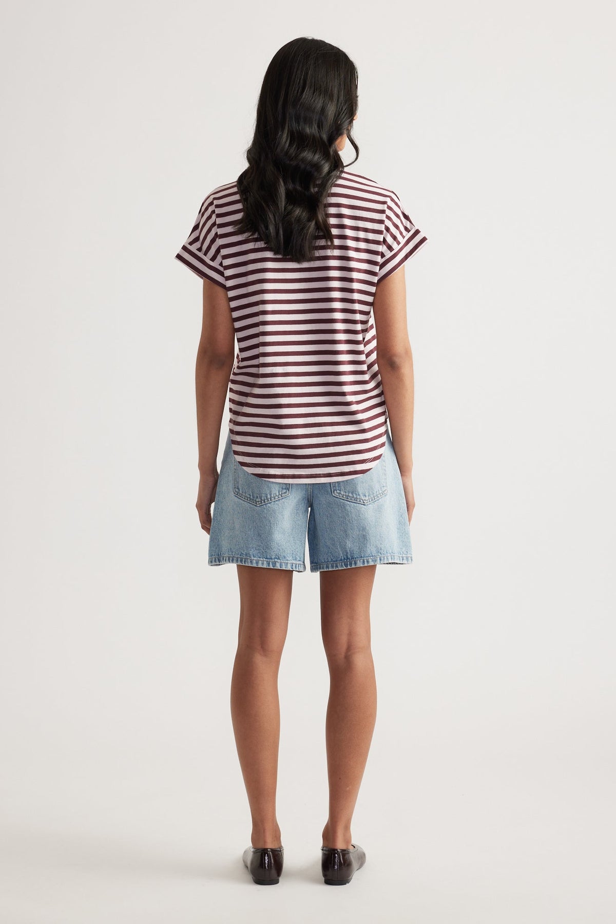 Rear view of woman wearing relaxed fit light blue denim shorts paired with a maroon and white striped rolled-cuff tee