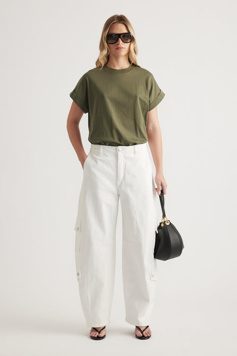 Woman wearing an olive green crew neck tee with white wide leg pants, sunglasses and a black handbag