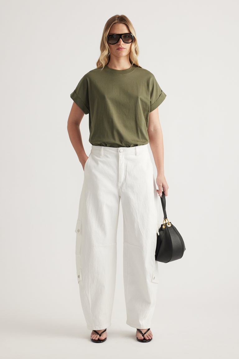 Woman wearing an olive green crew neck tee with white wide leg pants, sunglasses and a black handbag