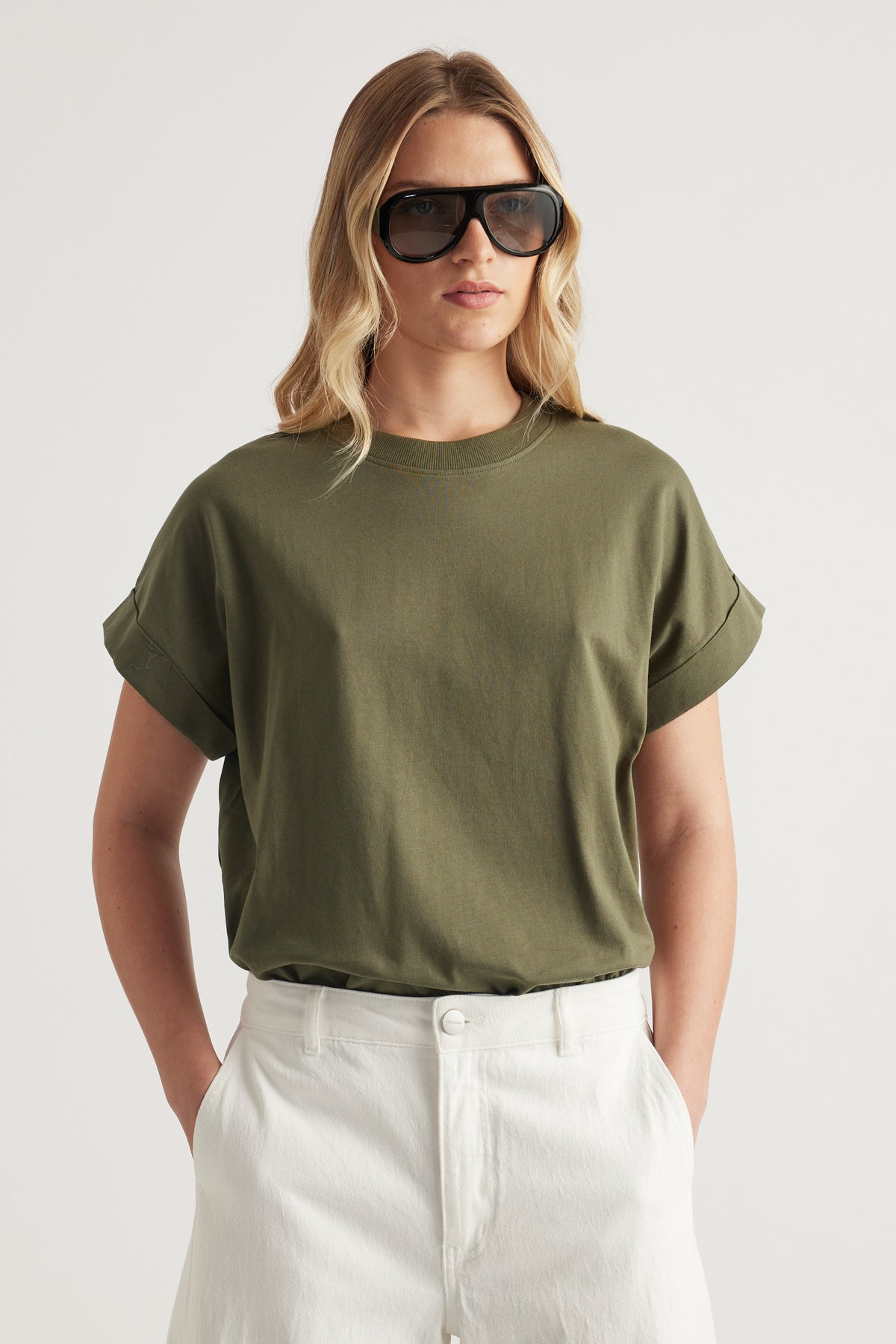 Woman wearing an olive green rolled cuff crew neck tee with white jeans and oversized sunglasses