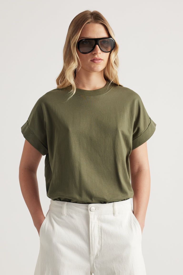 Woman wearing an olive green rolled cuff crew neck tee with white jeans and oversized sunglasses