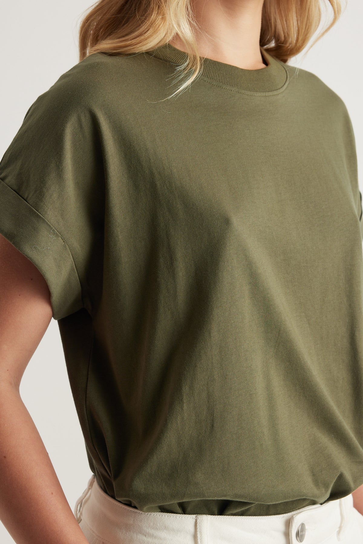 Woman wearing an olive green crew neck tee with rolled cuffs and white pants