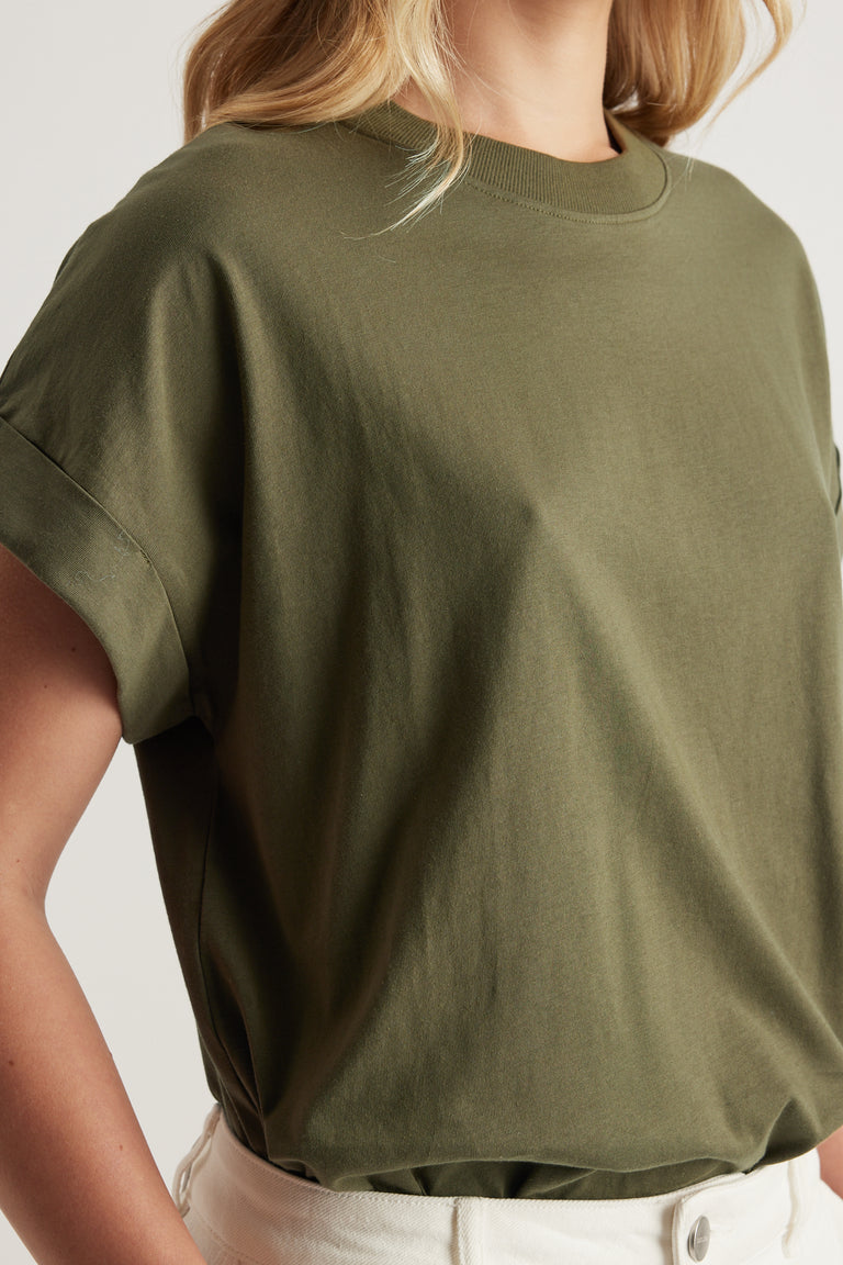 Woman wearing an olive green crew neck tee with rolled cuffs and white pants