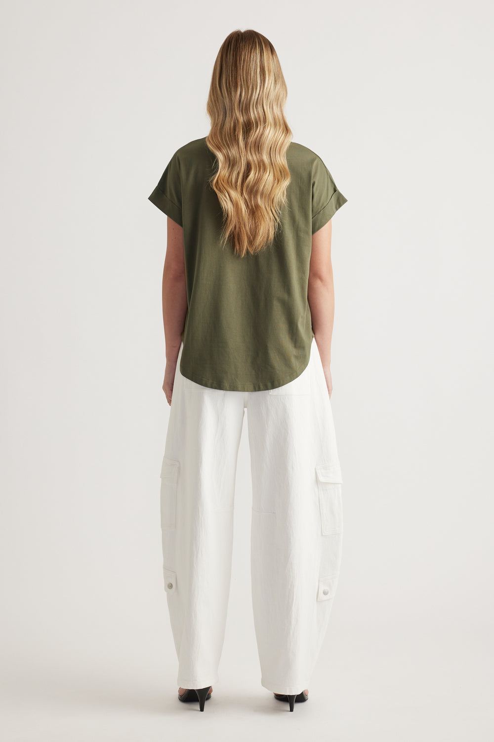 Woman seen from behind wearing an olive green tee, white cargo pants and black heels
