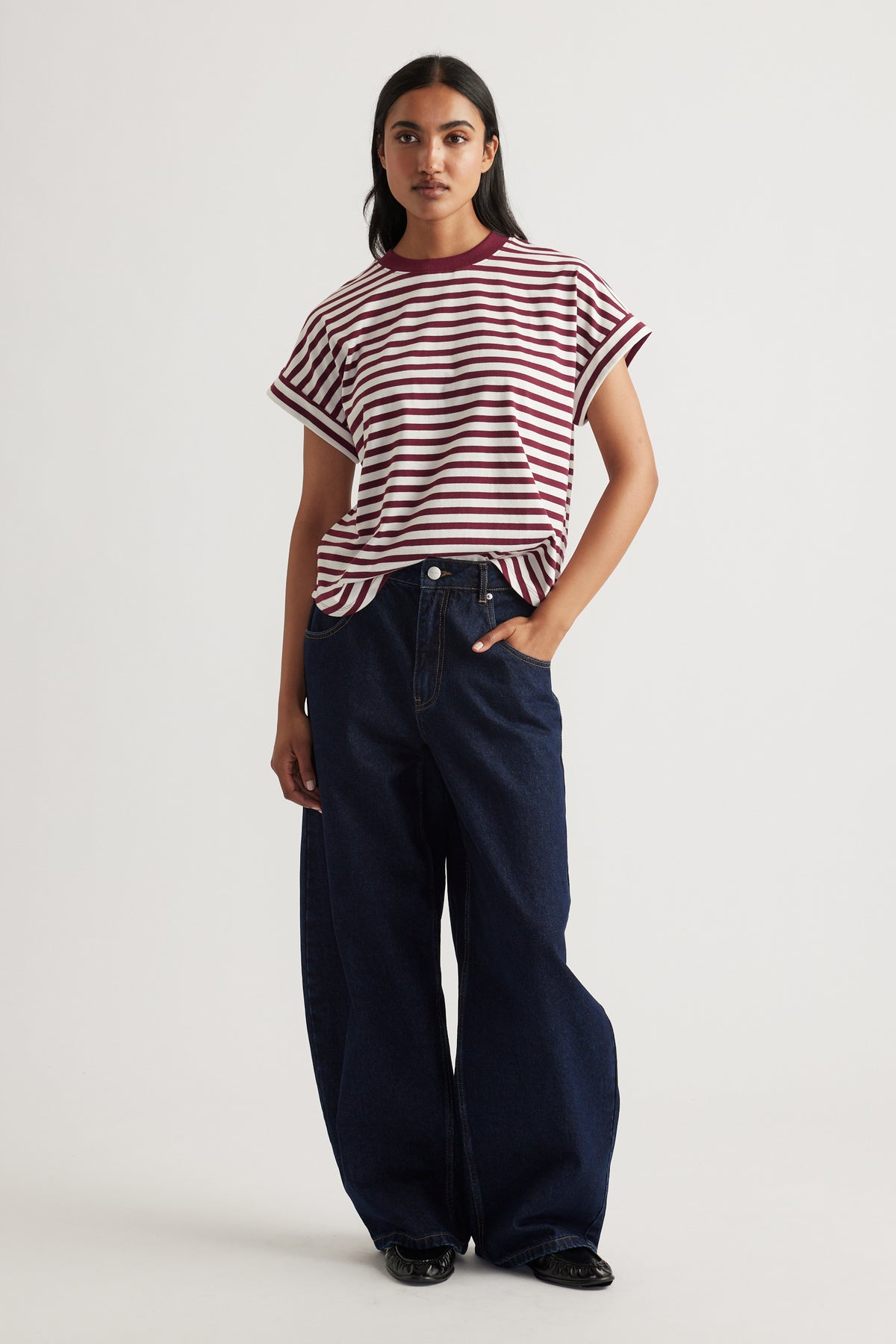 Woman wearing a relaxed fit ruby red and white striped tee paired with wide-leg dark denim jeans and black shoes