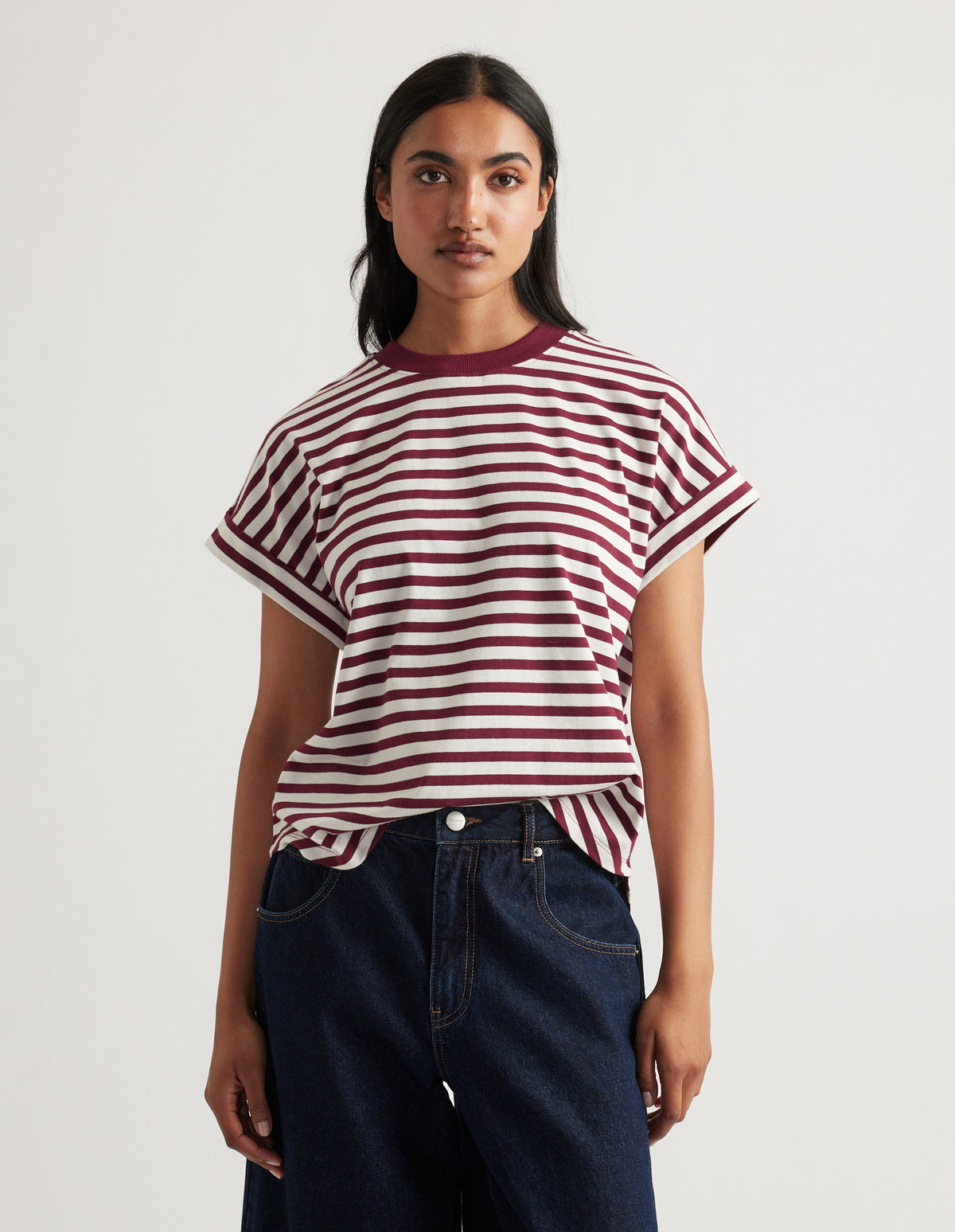 Woman wearing a relaxed fit crew tee with burgundy and white stripes paired with dark blue denim jeans