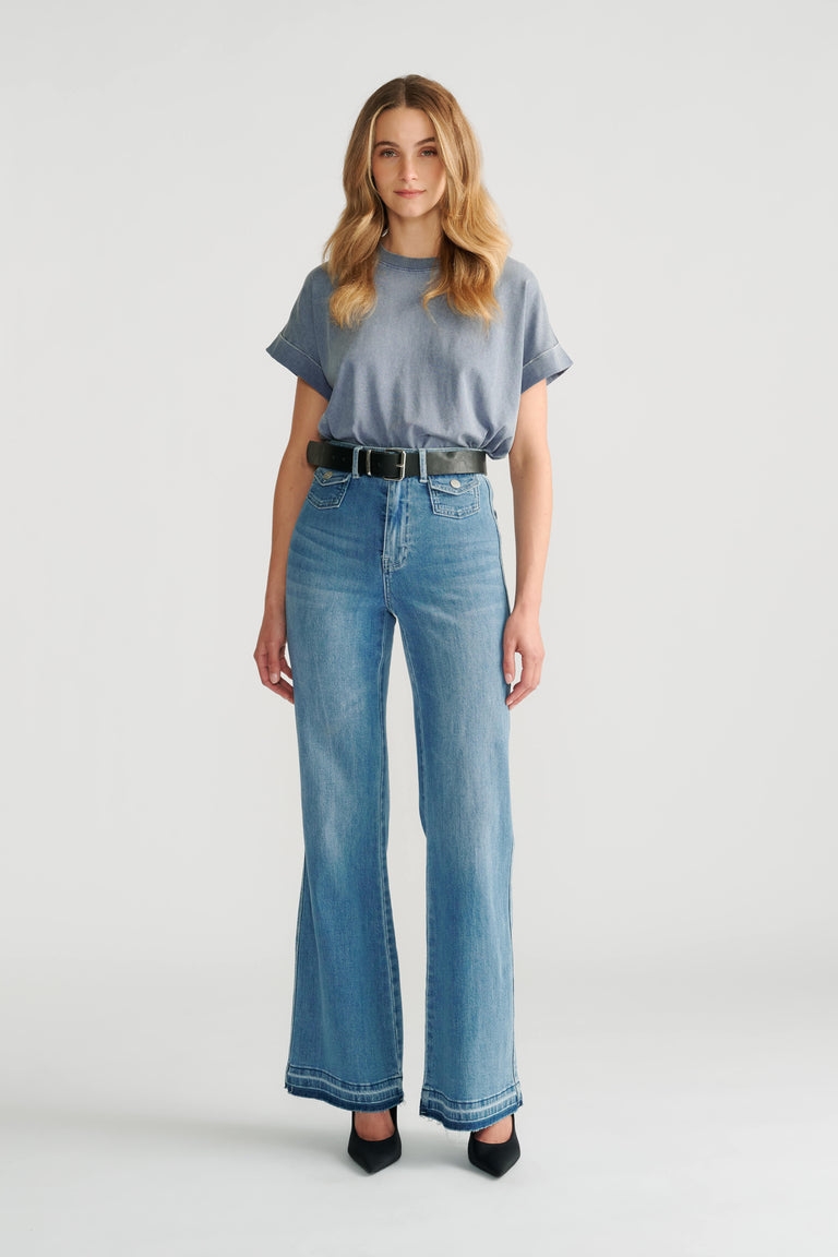 Woman wearing a soft blue crew neck tee tucked into high-waisted wide-leg light wash denim jeans with black belt and heels.