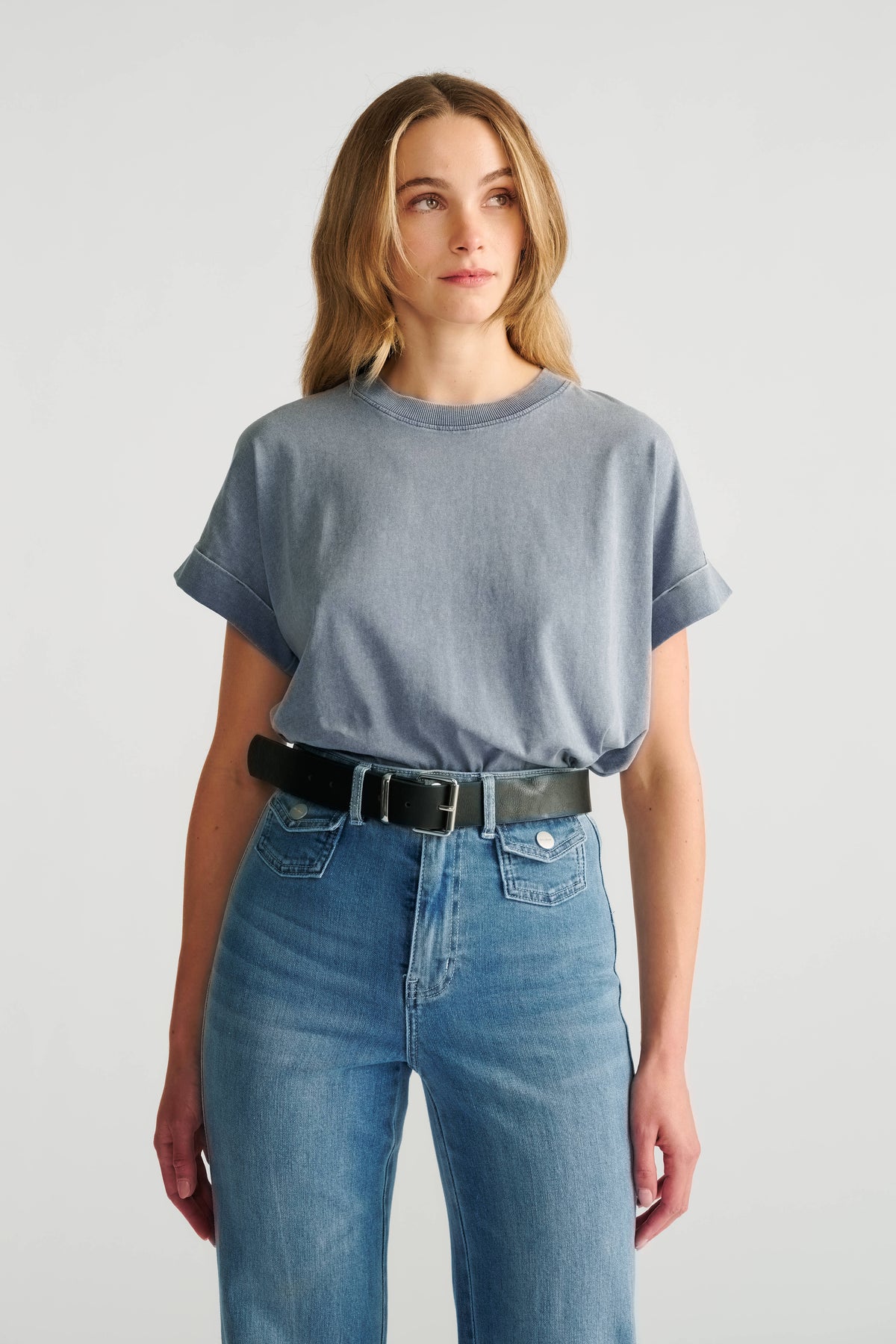 Woman wearing a relaxed blue crew neck tee with rolled sleeves tucked into high-rise light blue jeans and a black belt.