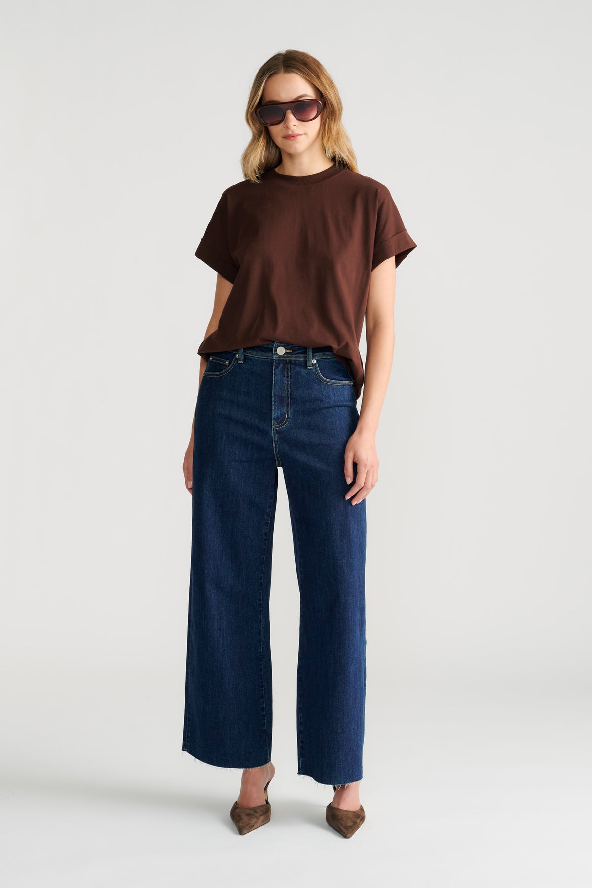 Woman wearing a relaxed fit brown crew neck tee paired with high-rise wide-leg dark denim jeans and brown pointed shoes.