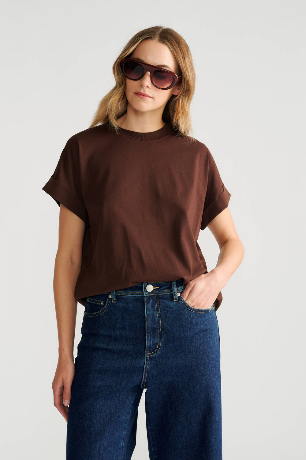 Woman wearing a relaxed fit crew neck tee in warm brown with rolled sleeves paired with dark high-rise wide-leg jeans.