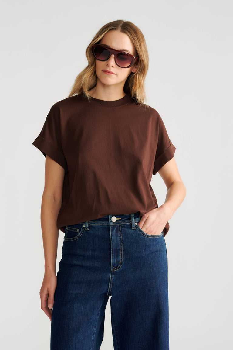 Woman wearing a relaxed fit crew neck tee in warm brown with rolled sleeves paired with dark high-rise wide-leg jeans.