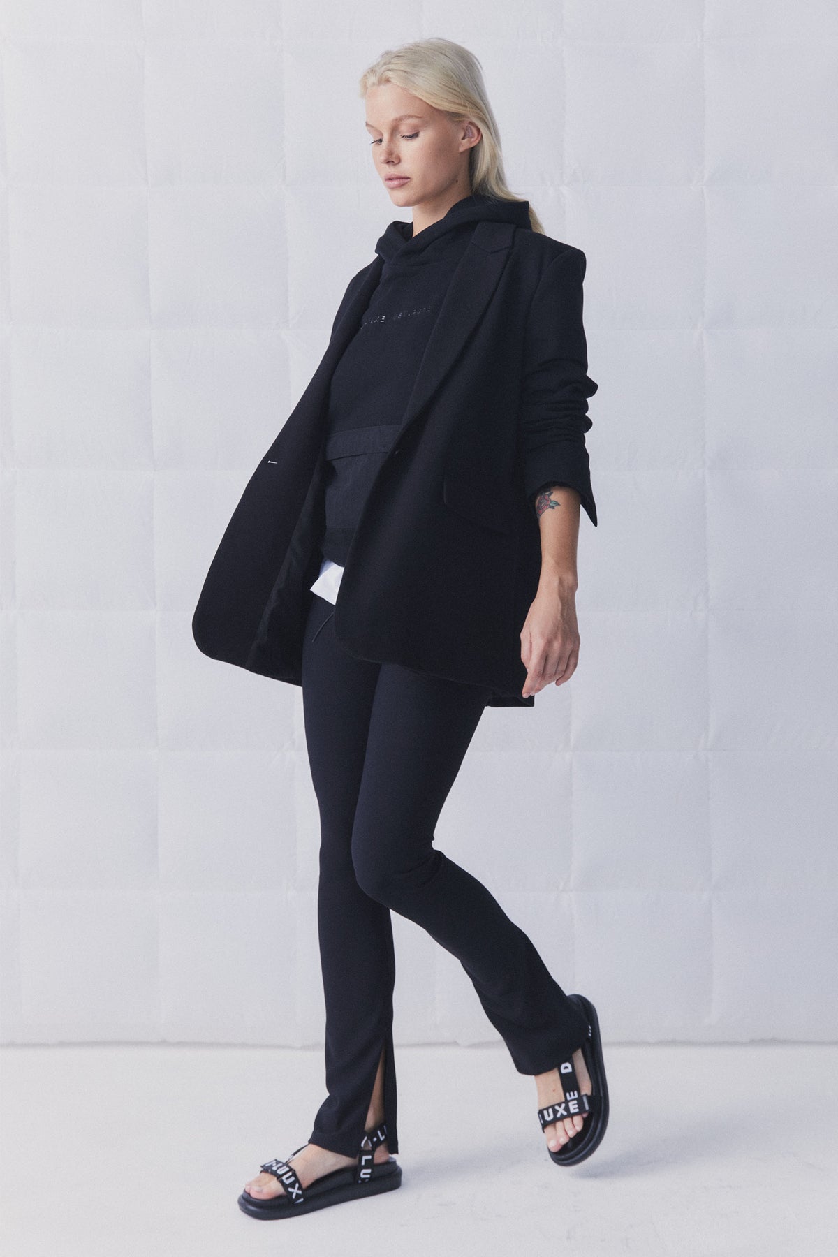 Woman wearing black slim-fit ribbed leggings with side splits paired with a layered black blazer and hoodie ensemble