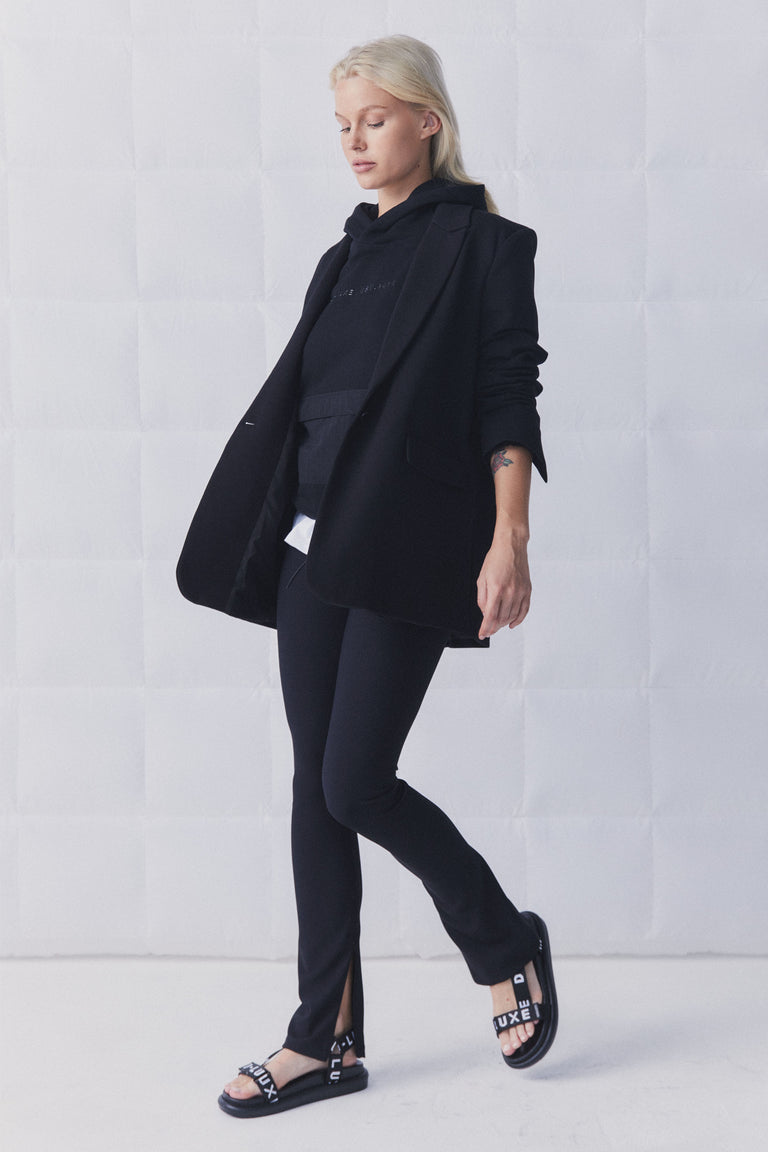 Woman wearing black slim-fit ribbed leggings with side splits paired with a layered black blazer and hoodie ensemble