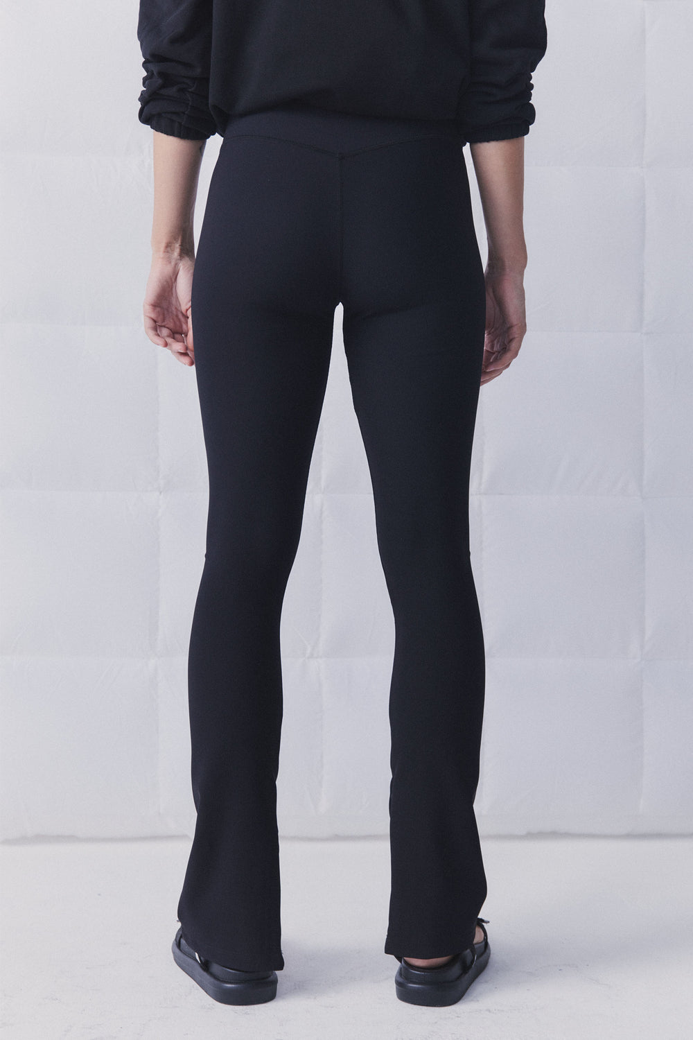 Rear view of black ribbed leggings with a subtle split hem, styled with a relaxed black top and flats