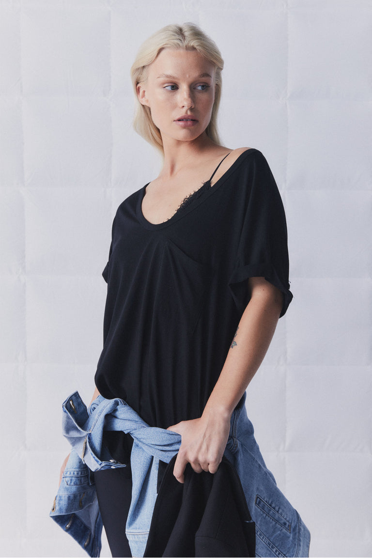 Woman wearing a relaxed black top layered over a delicate lace bralette, styled with a tied denim jacket around the waist.