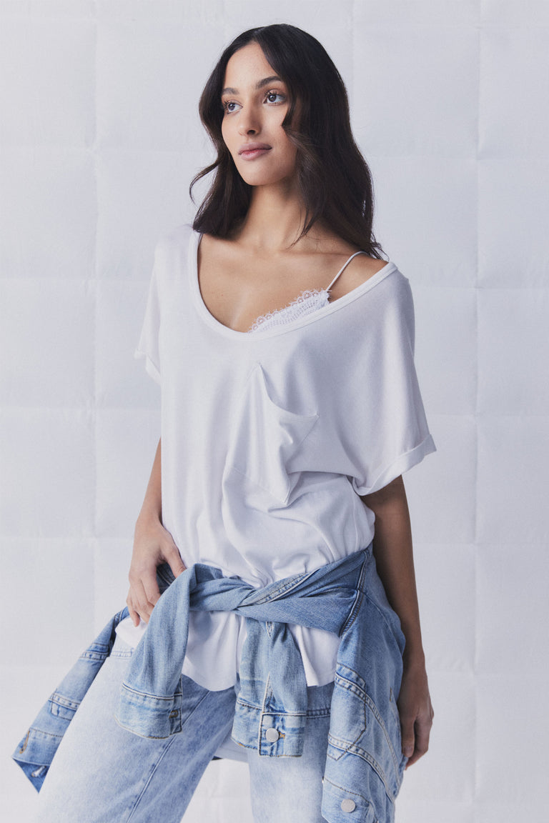 Woman wearing a relaxed white tee showing delicate lace bralette strap, with light washed denim jacket tied at waist and jeans