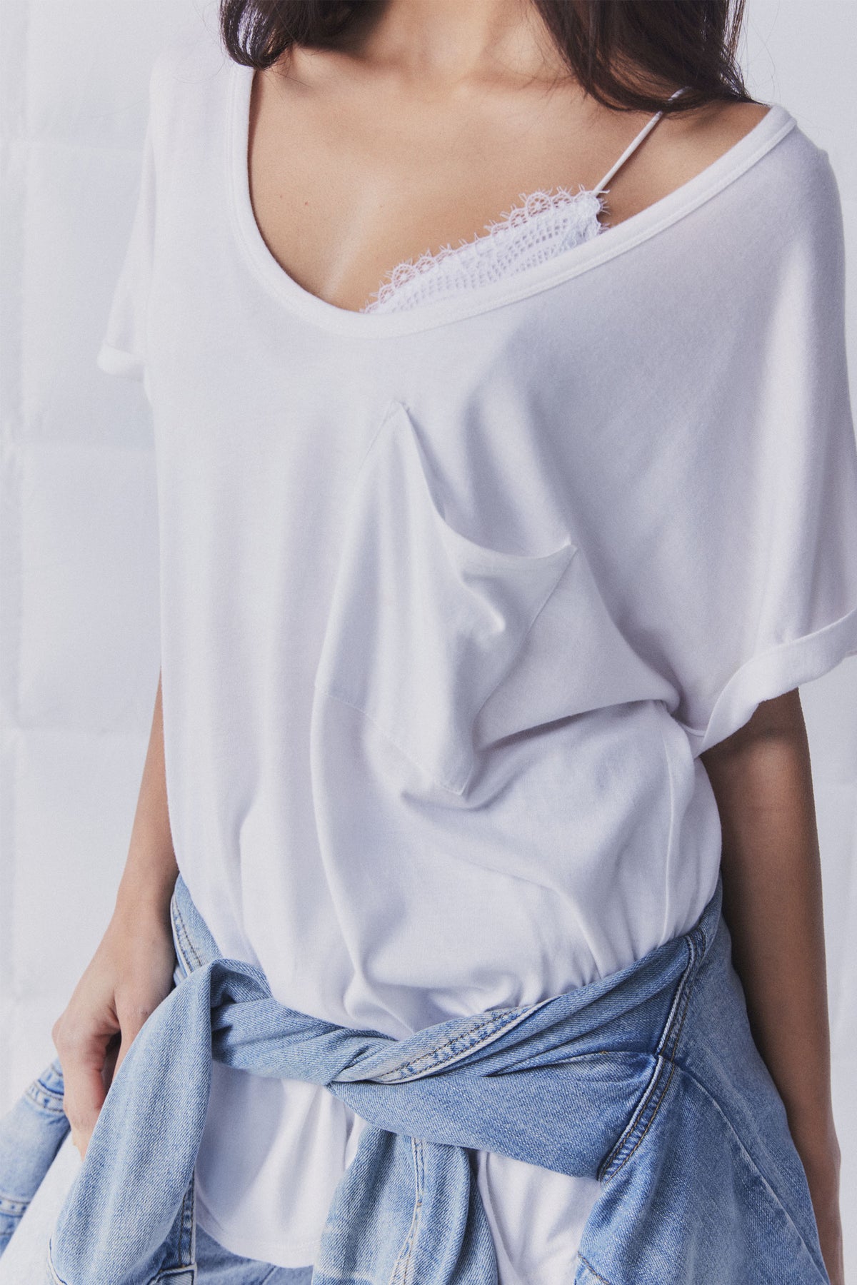 White relaxed-fit tee with a scooped neckline revealing delicate lace bralette, styled with light denim jacket tied at waist.