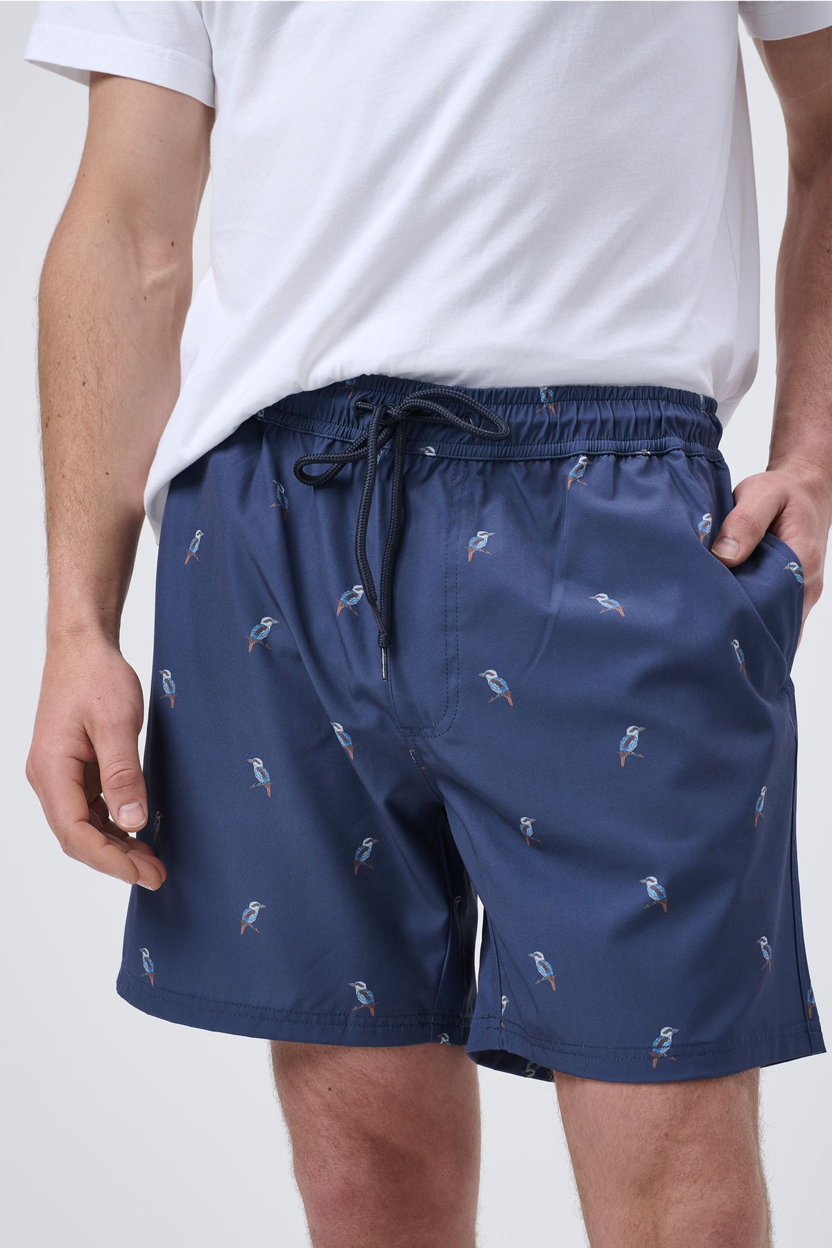 Navy men's swim shorts with small bird prints, elastic waistband, and drawstring, styled with a white t-shirt