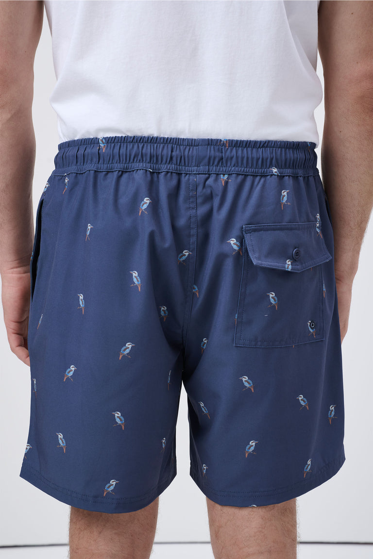 Back view of navy men's swim shorts with small bird print and a buttoned pocket, worn with a white shirt