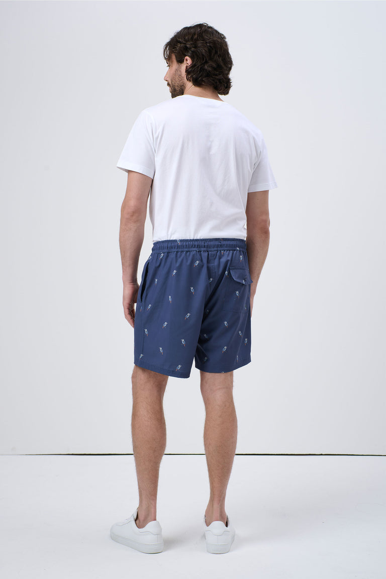 Man wearing navy blue swim shorts with small colorful pattern, paired with plain white t-shirt and white sneakers, back view