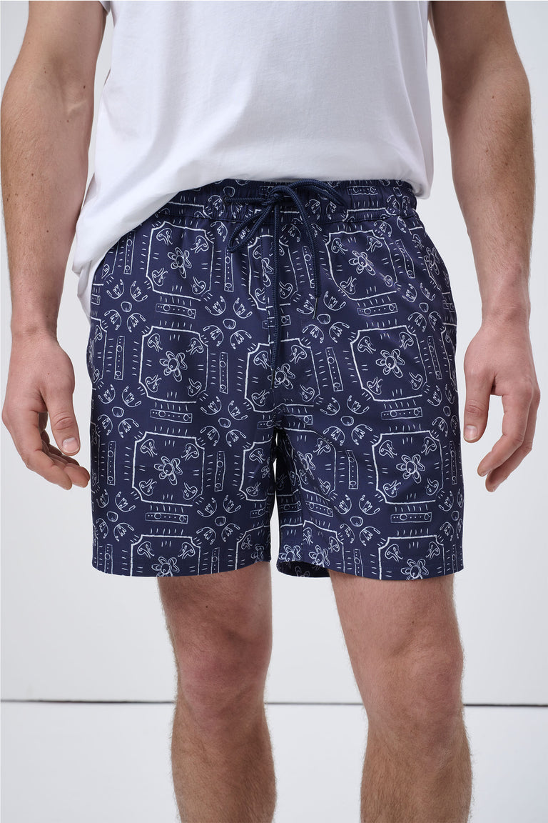 Man wearing navy swim shorts with white abstract geometric print and drawstring waist paired with plain white tee