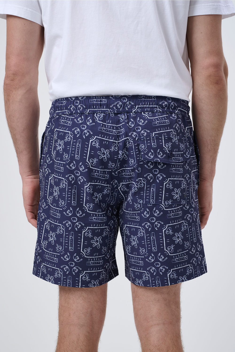 Rear view of navy swim shorts with white abstract floral and geometric print worn with a white t-shirt