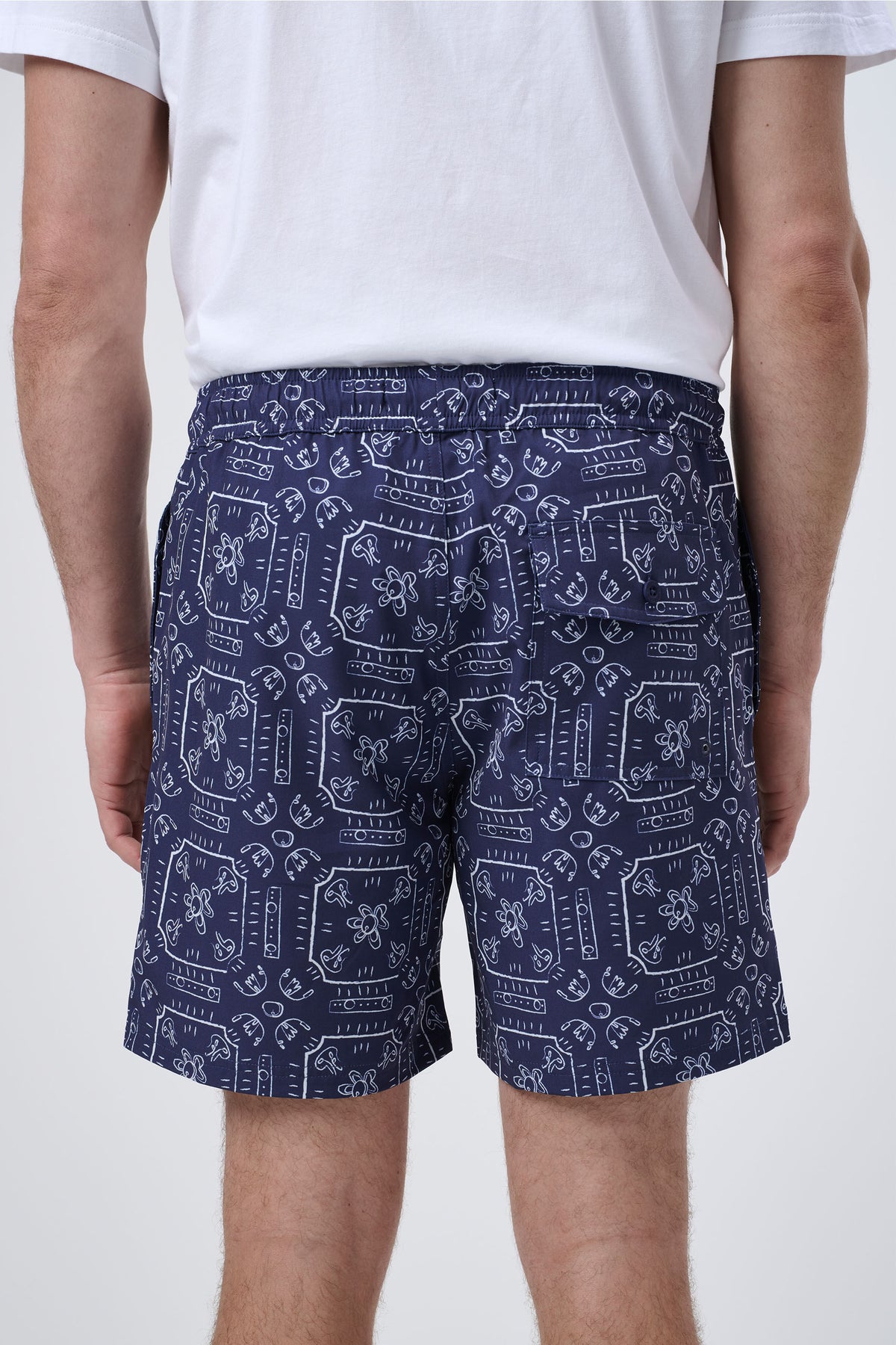 Rear view of navy swim shorts with white abstract floral and geometric print worn with a white t-shirt